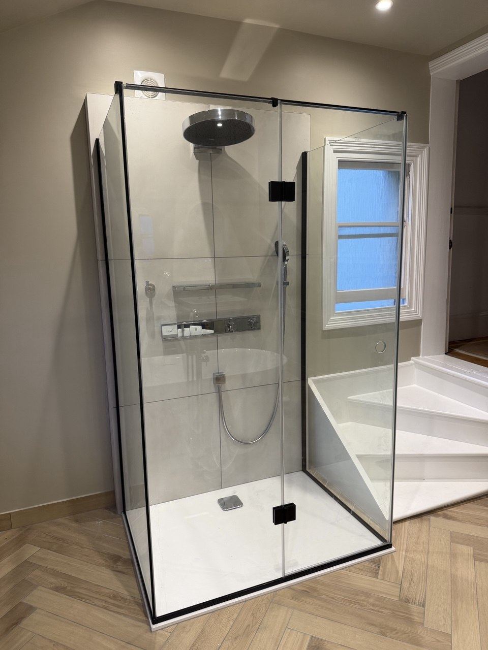 A frameless glass shower enclosure with large-format porcelain walls on a wood-effect herringbone floor