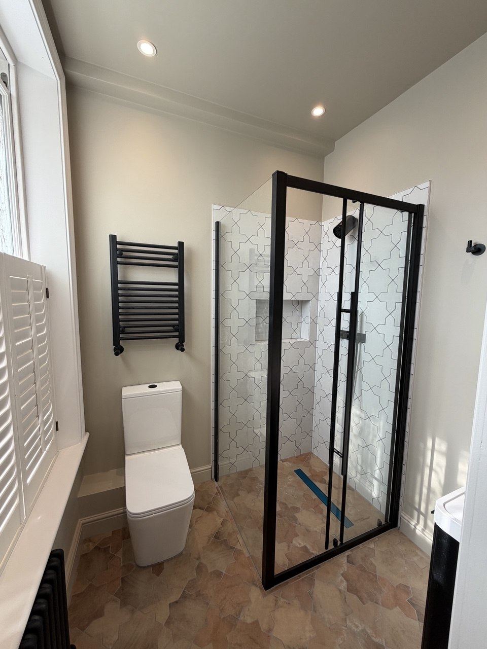 A shower in white star-and-cross pattern tiles with a niche, a black-framed enclosure and terracotta-effect floor tiles