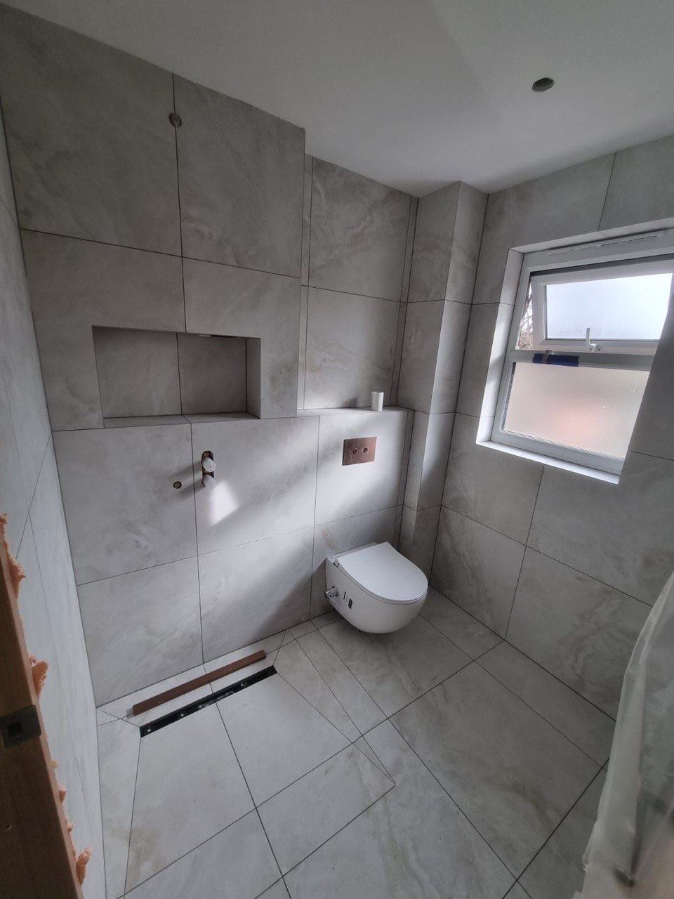 A wet room in large-format marble-effect porcelain with a linear drain, a recessed niche and a wall-hung WC